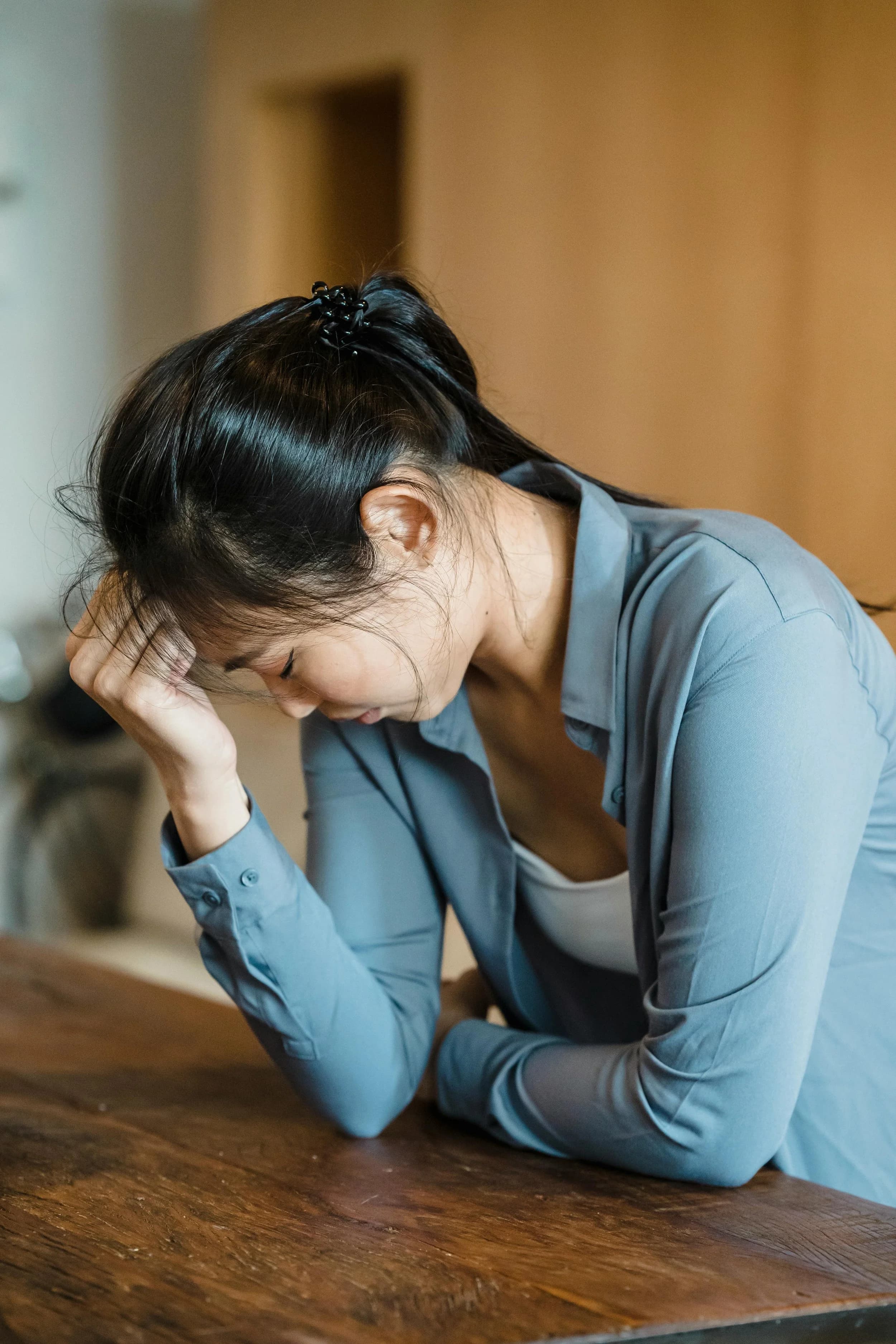 A woman resting her head on her hand at a wooden table, looking down