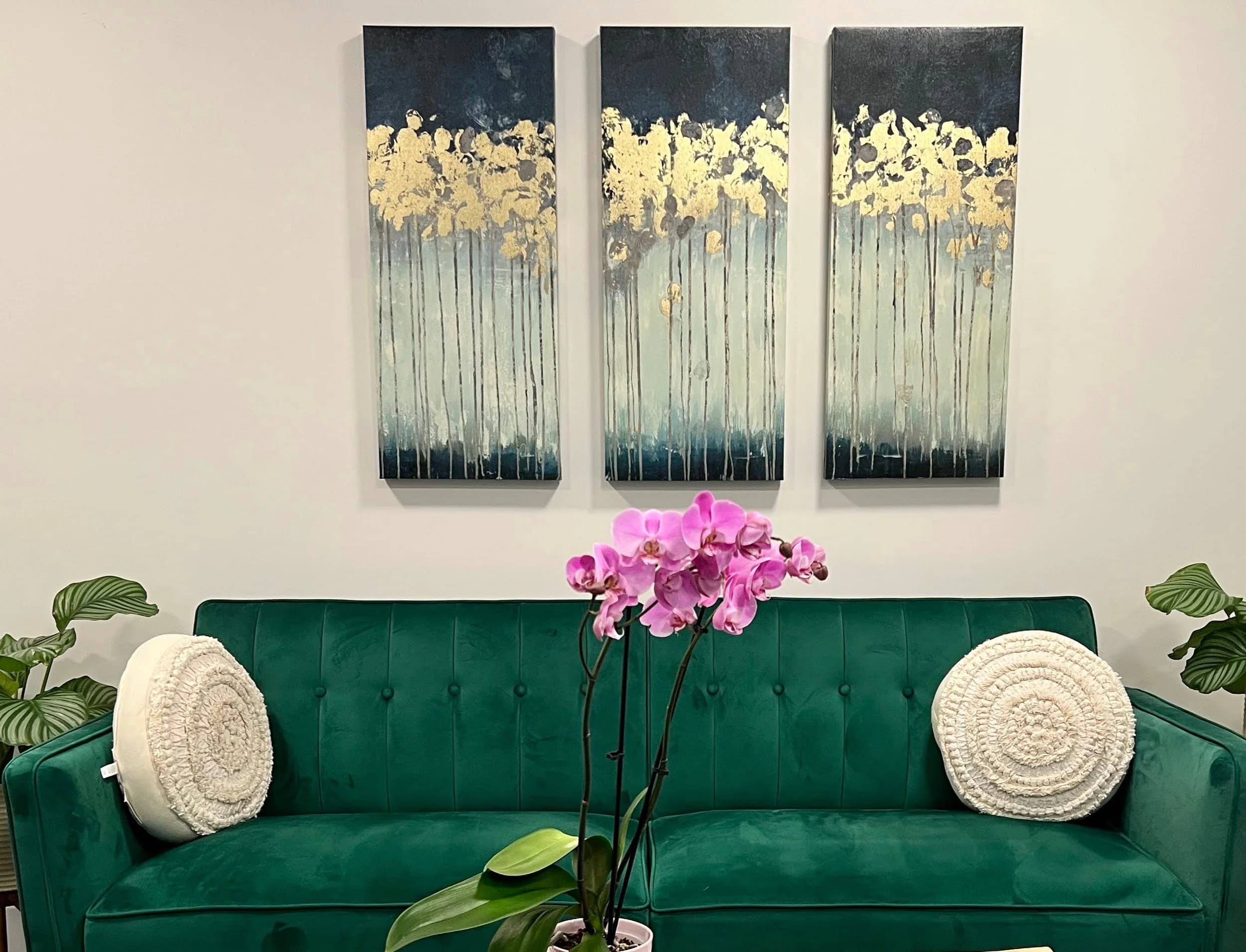A waiting room with a green velvet sofa, an orchid, and a three-panel painting
