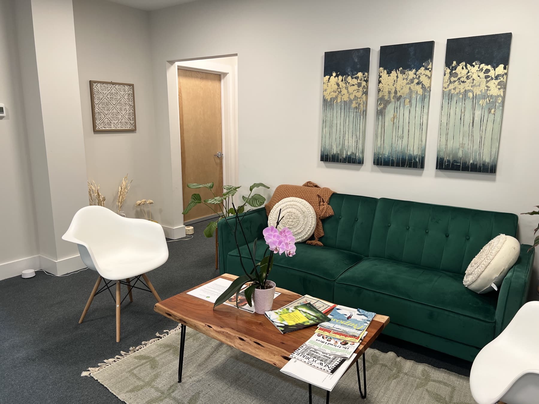 A warm therapy room with a sofa, an armchair, a reading lamp, and a window