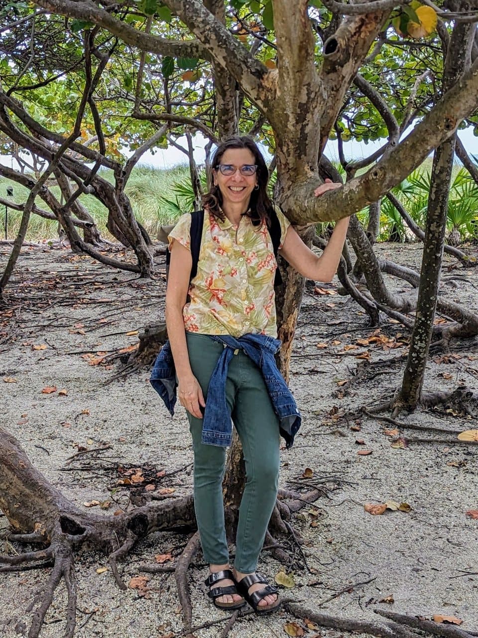Rebecca Gotterer standing among sculptural seaside trees on the sand