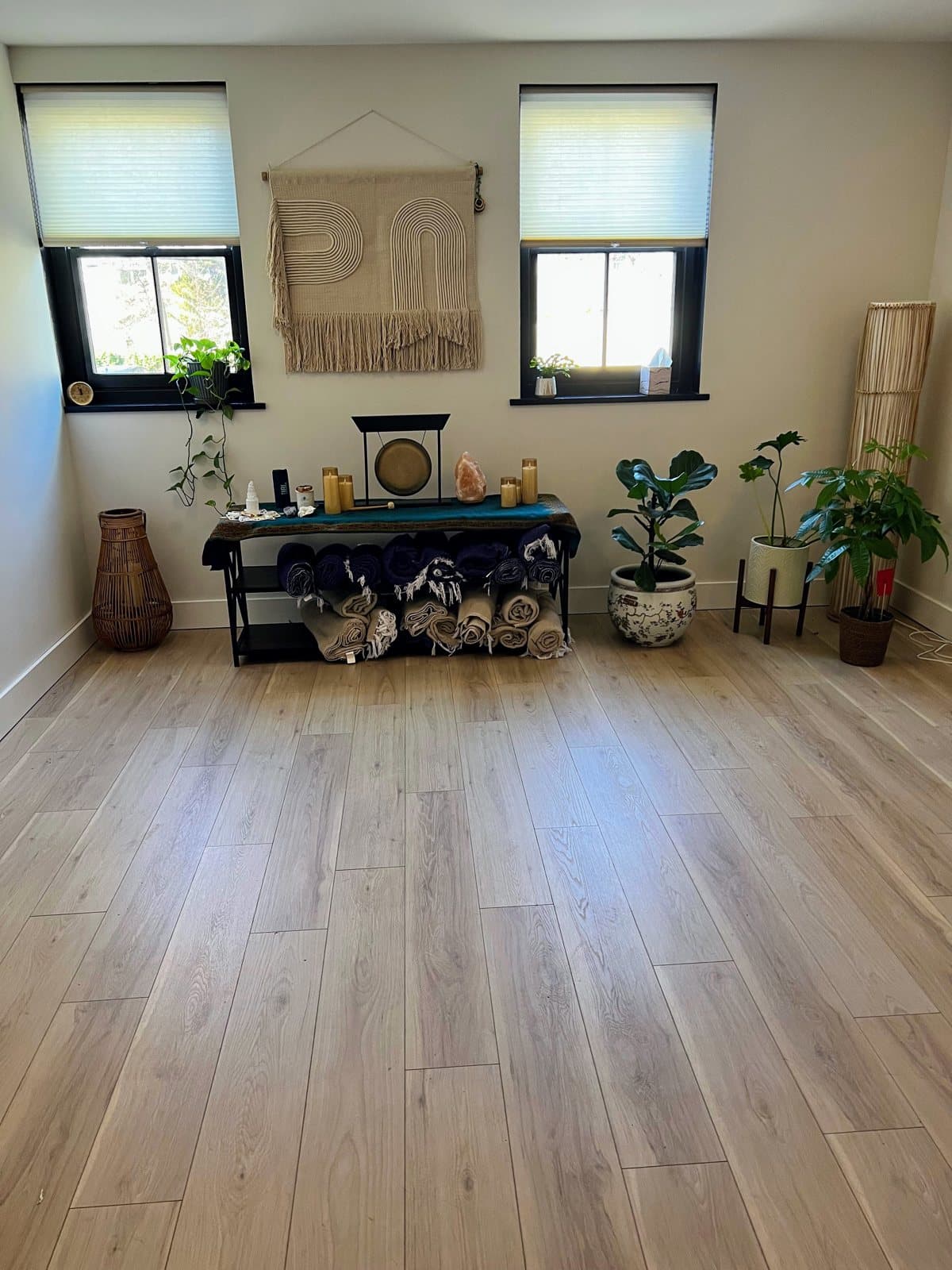 An open room with a wood floor, rolled blankets, plants, and a gong on a low table